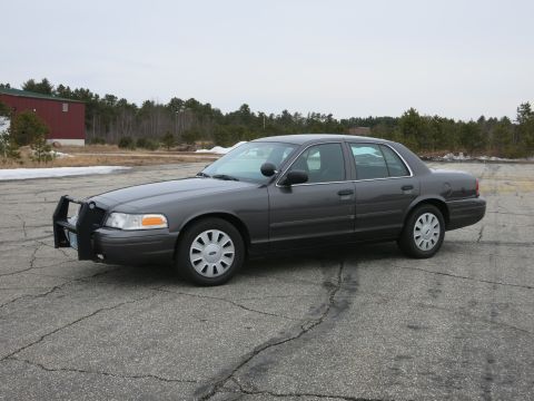 2001 Ford Crown Victoria - A dark grey 2001 Ford Crown Victoria, equipped with a push bar, is seen from a three-quarter front angle on a cloudy day.