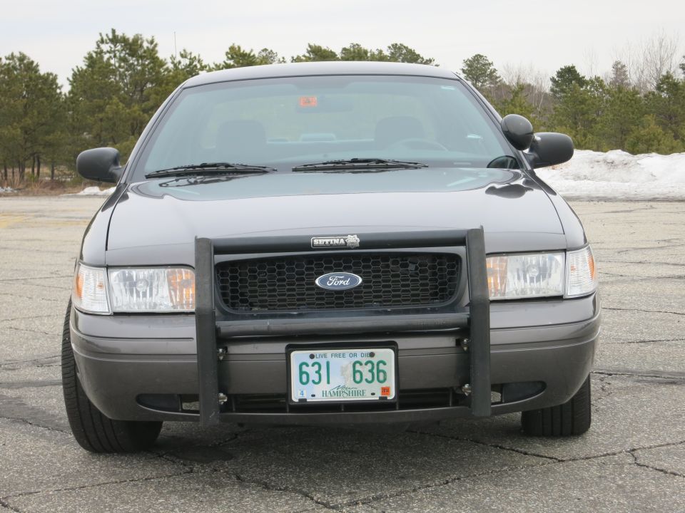 Front view of a grey Ford Crown Victoria with a push bar and police markings on the license plate