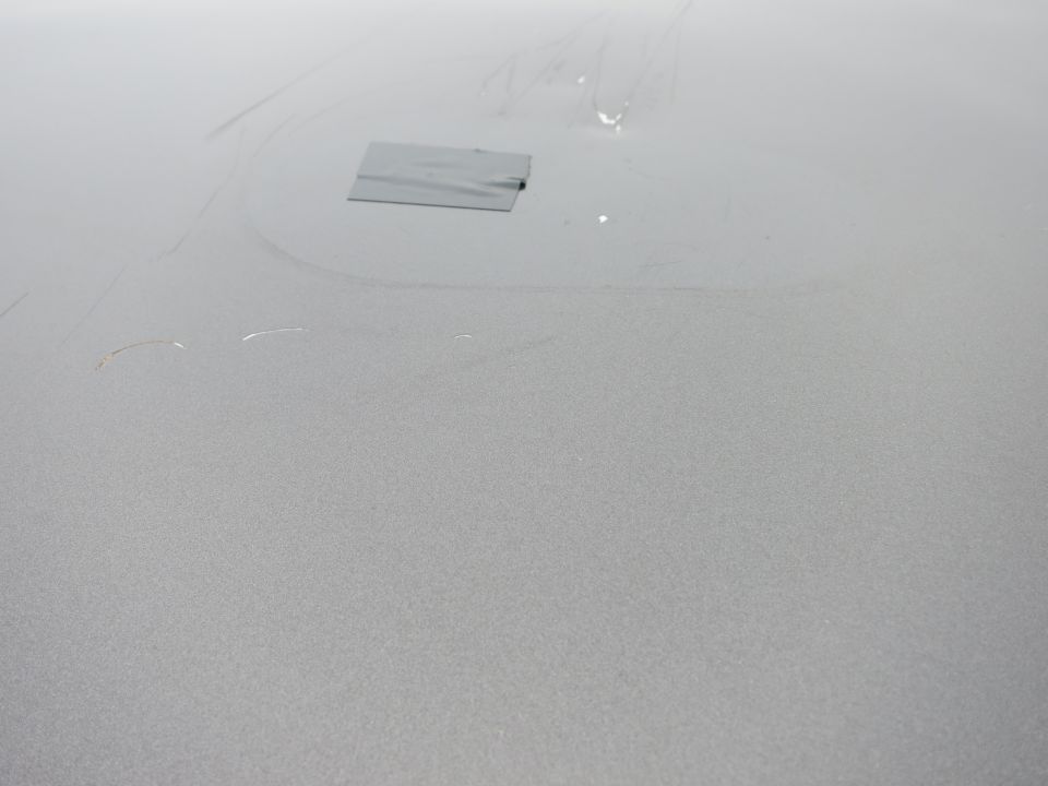Silver car hood with a piece of gray duct tape and some scratches