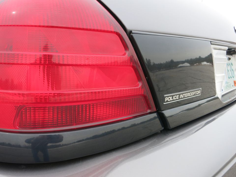 Rear quarter panel of a 2001 Ford Crown Victoria Police Interceptor, showing the taillight and "POLICE INTERCEPTOR" badge