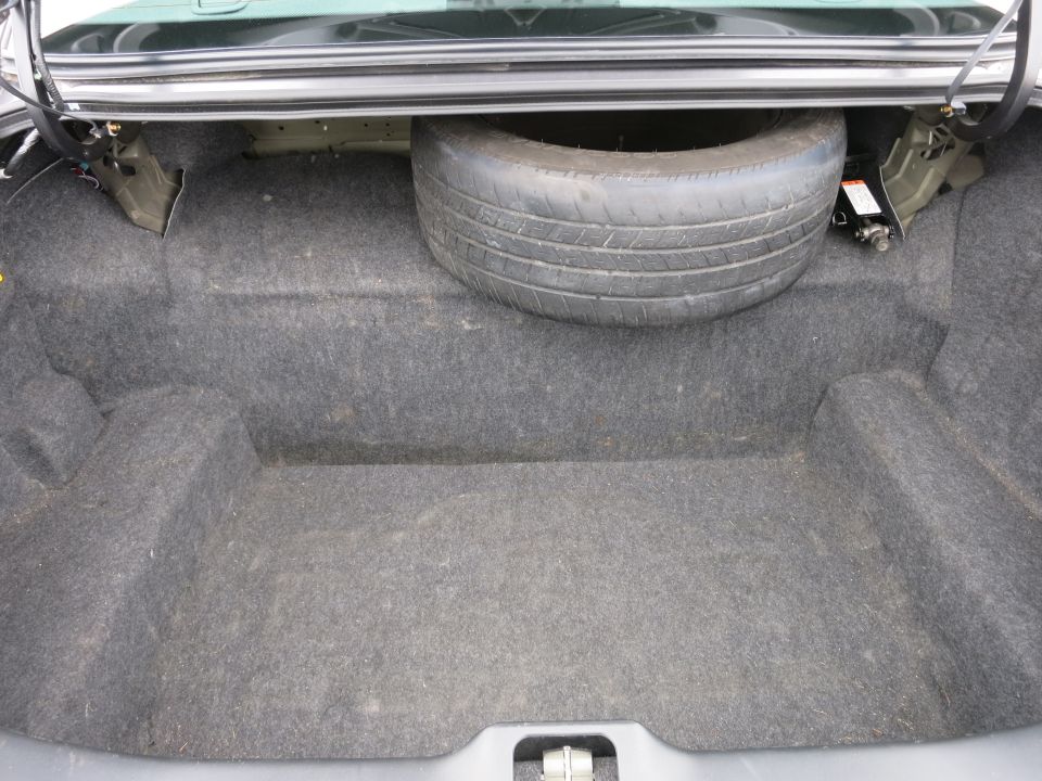 Car trunk interior with spare tire and jack. Gray carpet lining