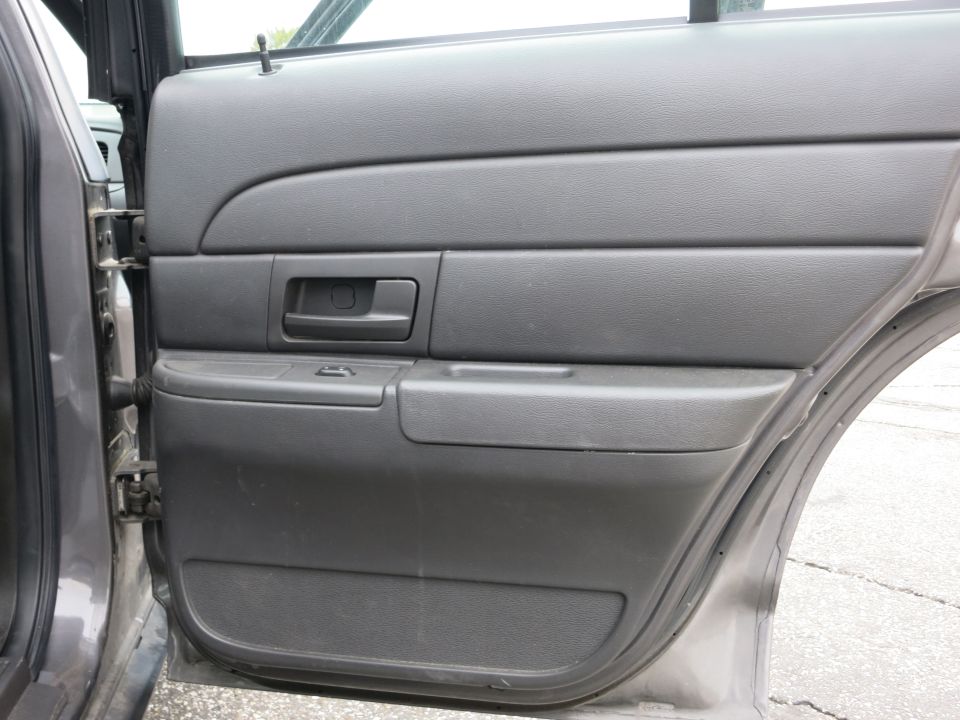 Interior shot of a gray car door panel with a black handle and window controls. The door is open, showing the car's interior