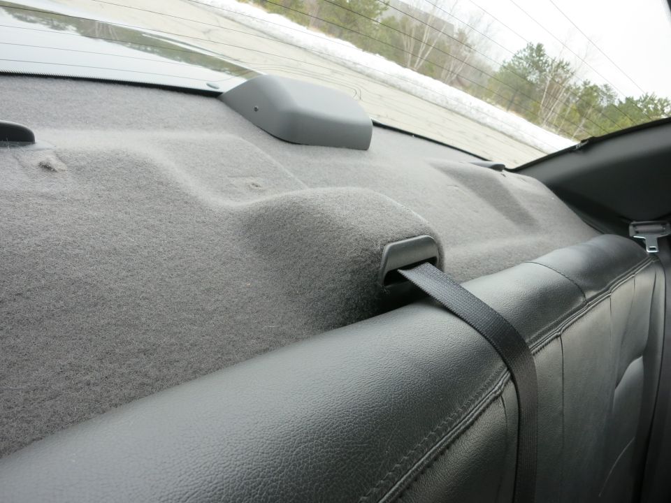 Car interior showing grey carpeted rear deck and black leather seat with seatbelt
