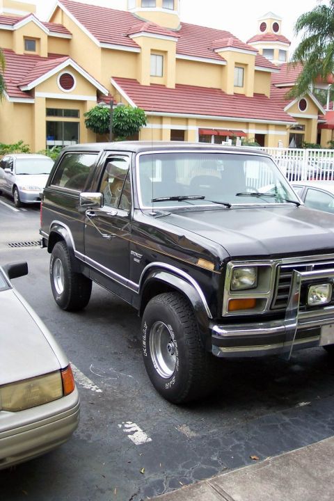 1986 Ford Bronco - A black Ford Bronco is parked in a lot next to another vehicle.