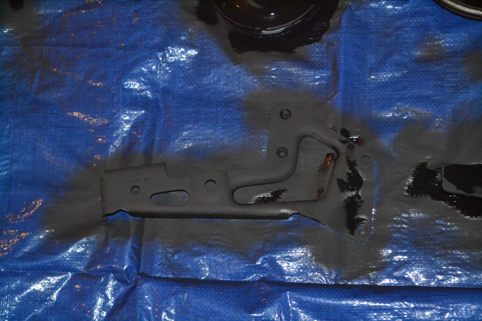 Metal bracket with holes and mounting points, placed on a blue tarp