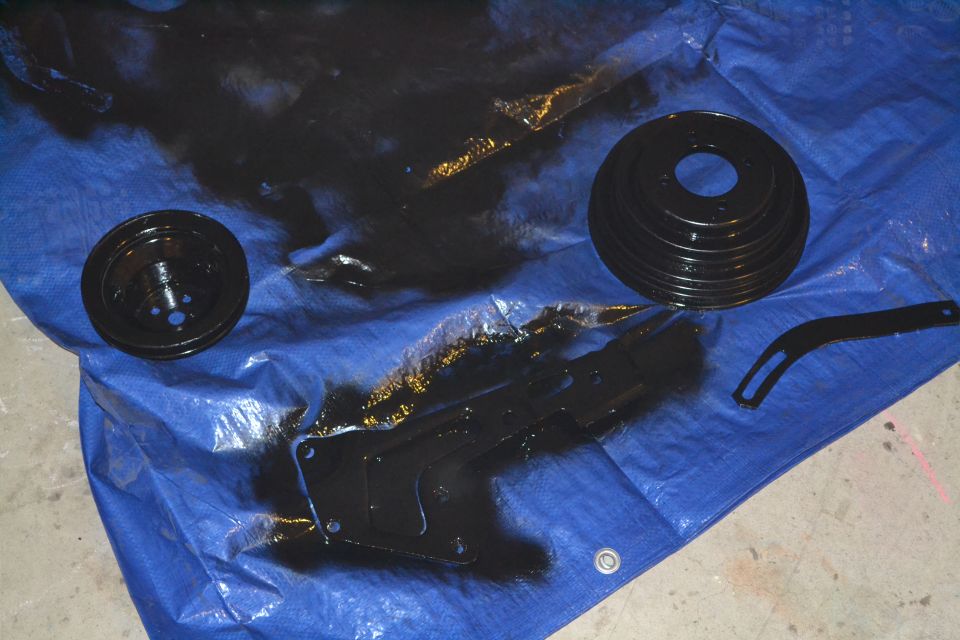 Black painted pulleys and bracket on a blue tarp with overspray