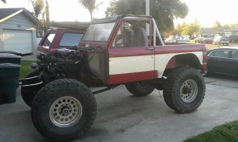 1968 Ford Bronco - A red and white 1968 Ford Bronco is shown with its engine exposed and lifted on large tires.