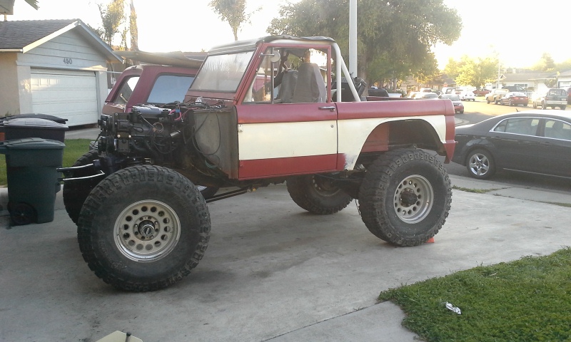 1968 Ford Bronco with engine exposed, red and white paint, lifted suspension, and large off-road tires