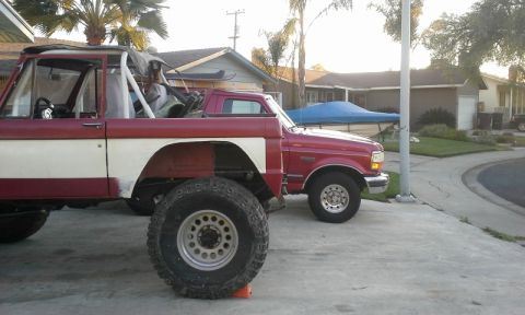 1968 Ford Bronco - A heavily modified off-road vehicle sits beside a red pickup truck in a residential driveway.