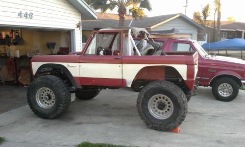 1968 Ford Bronco - A heavily modified Ford Bronco with oversized tires sits in a driveway next to a pickup truck.