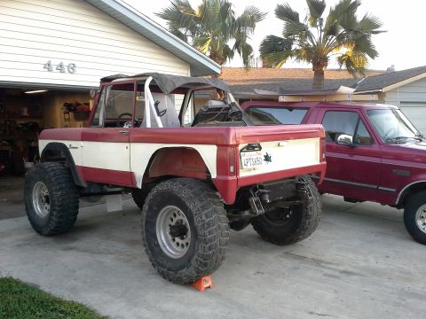 1968 Ford Bronco - A modified red and white Ford Bronco is parked next to a maroon Ford truck in a suburban driveway.