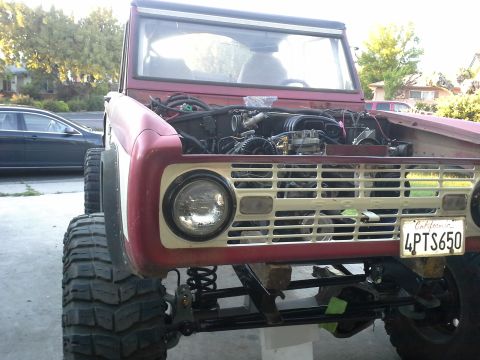 1968 Ford Bronco - The engine bay of a 1968 Ford Bronco is visible, with large tires and a California license plate.