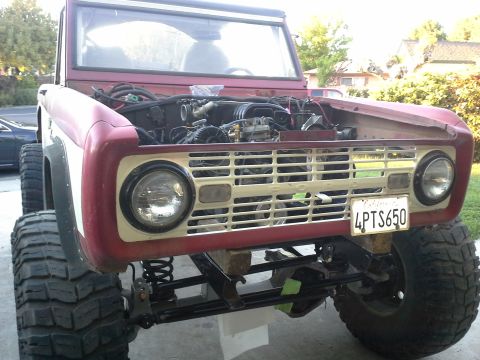 1968 Ford Bronco - A red 1968 Ford Bronco is shown from the front with its hood open, revealing the engine and large off-road tires.