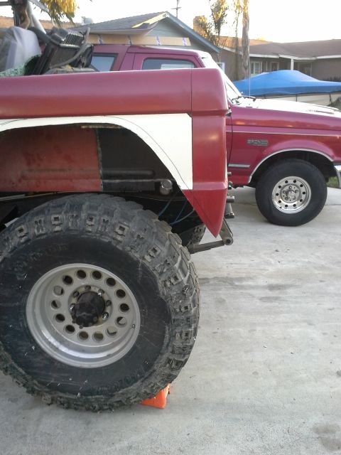 1968 Ford Bronco - Two pickup trucks are parked on a concrete surface, one in the foreground with large tires and a two-tone paint scheme.