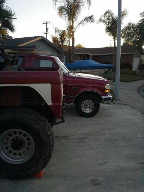 1968 Ford Bronco - Two red trucks are parked on a driveway, with one in the foreground large off-road tires.