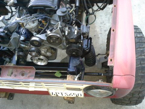 1968 Ford Bronco - Close-up of vehicle engine and front suspension components, with a red fender and license plate visible.
