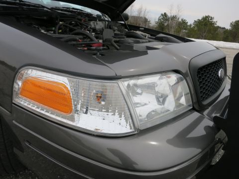2001 Ford Crown Victoria - The front corner of a 2001 Ford Crown Victoria is visible with the hood raised, revealing the engine compartment.