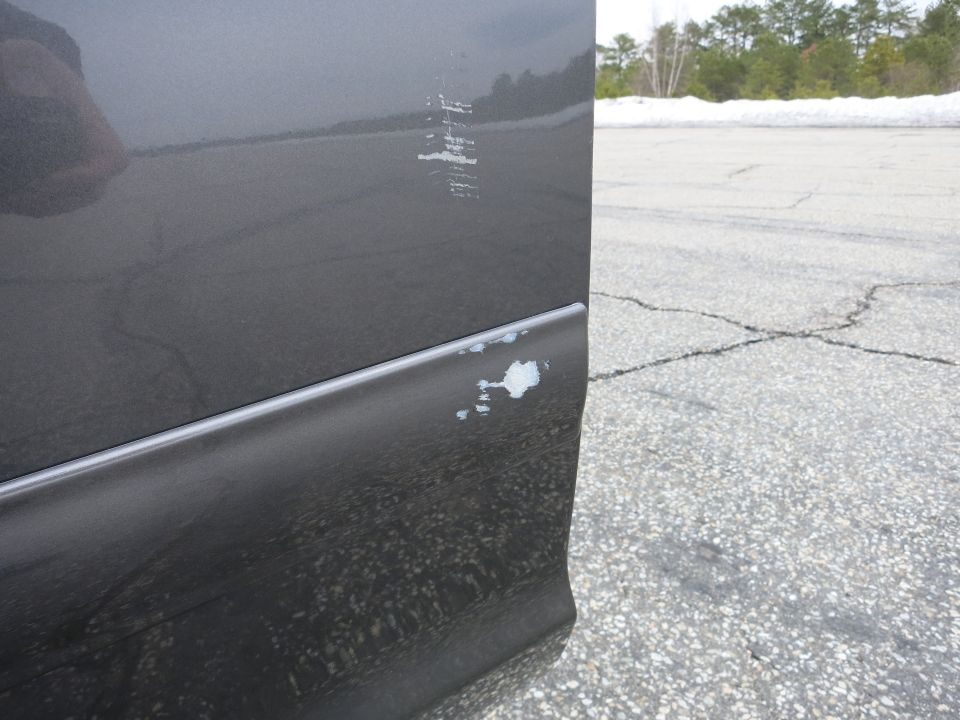 Close-up of a dark gray car door with scratches and chipped paint near the bottom trim