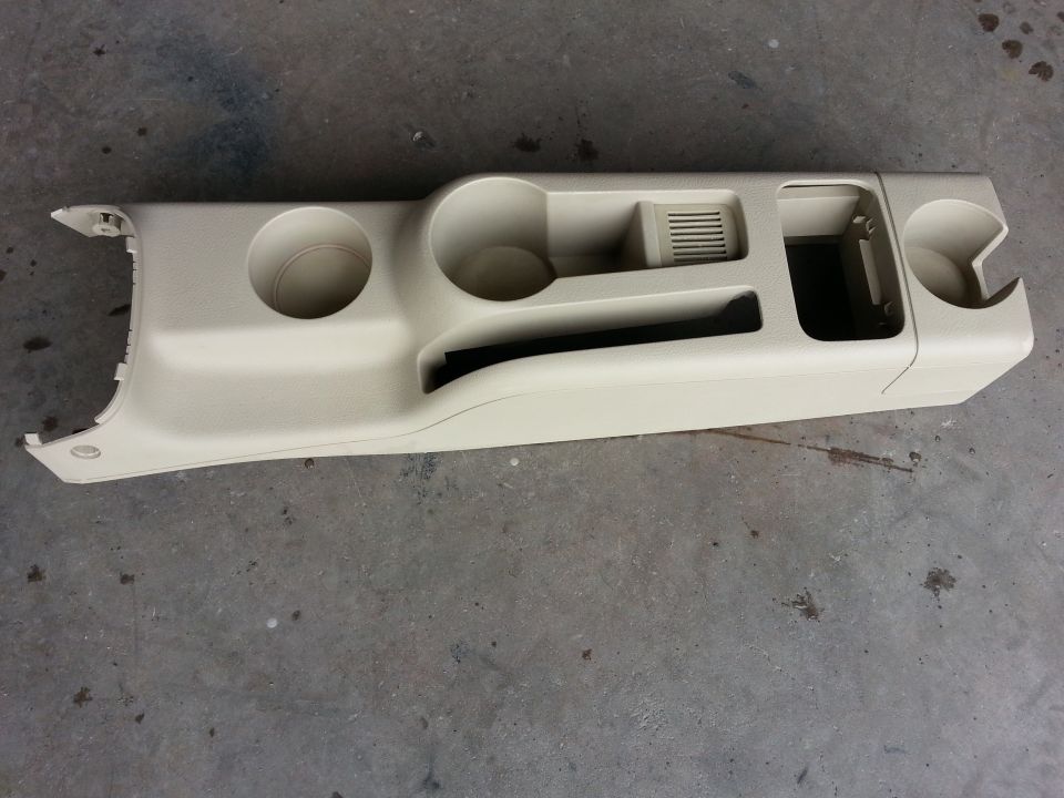 Beige plastic center console trim with two cup holders, a vent, and storage compartments