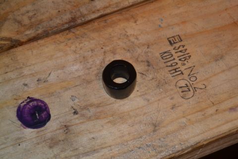 1981 Ford F-250 - A single black rubber bushing rests on a wooden surface next to a purple stain and stamped markings.