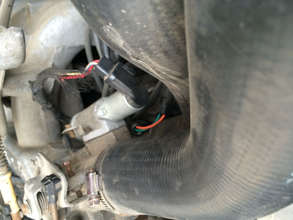 Engine bay with hoses and electrical connectors. A black connector with red, white, and black wires is visible