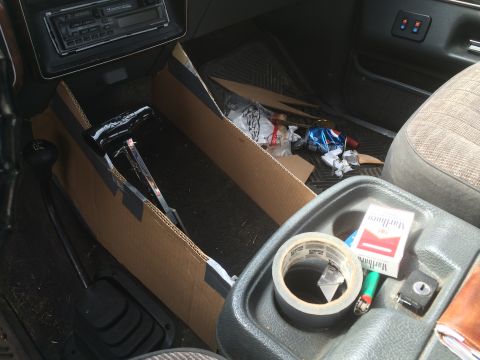 1991 Ford F-150 - The interior of a truck shows a custom cardboard console insert with trash and a pack of Marlboro cigarettes.
