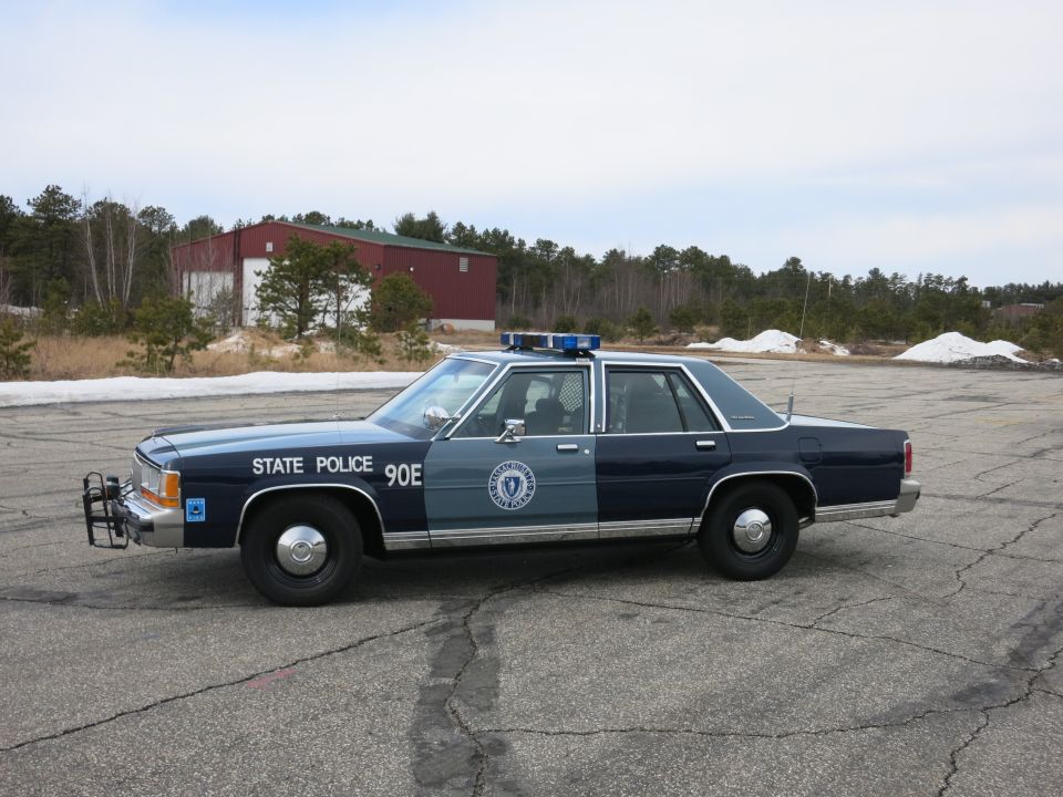 Massachusetts State Police Ford sedan, front three-quarter view near red barn