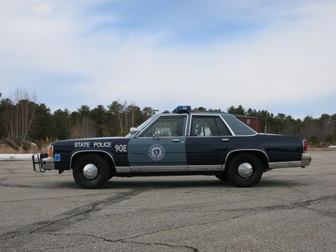 1991 Ford LTD Crown Victoria - navy-and-gray Massachusetts State Police Ford cruiser shown in driver-side profile on an open paved lot under a clear sky.