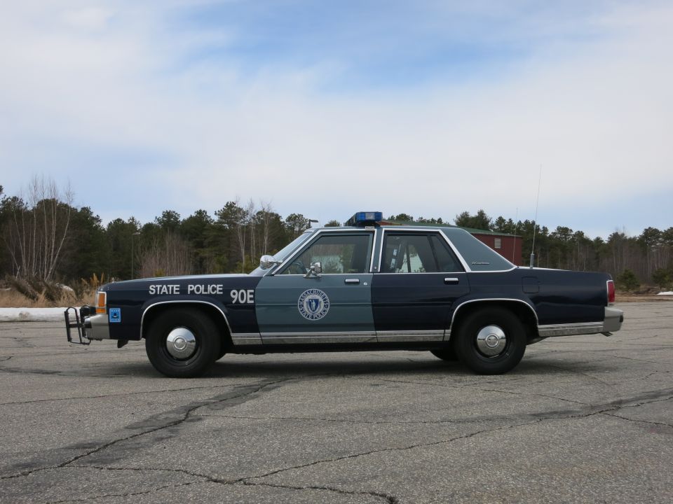 Massachusetts State Police Ford sedan, driver-side profile under blue sky