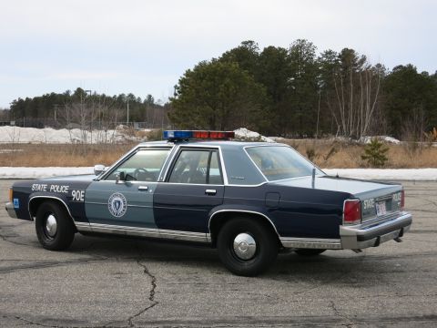 1991 Ford LTD Crown Victoria - Driver-side rear three-quarter view of a navy-and-gray Massachusetts State Police Ford cruiser with STATE POLICE markings and light bar.