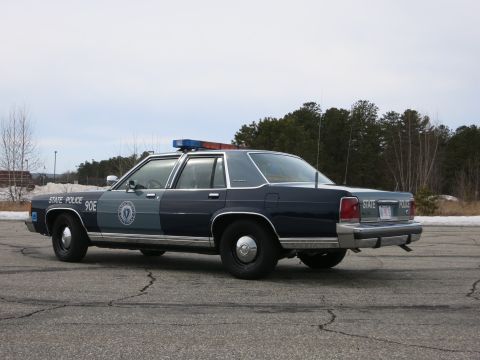 1991 Ford LTD Crown Victoria - Driver-side rear three-quarter view of a navy-and-gray Massachusetts State Police Ford cruiser with red light bar and MA plate.