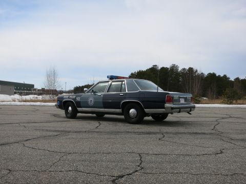 1991 Ford LTD Crown Victoria - two-tone Massachusetts State Police Ford cruiser seen at distance in rear three-quarter on an open paved lot near a metal building.