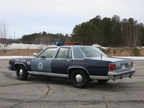 1991 Ford LTD Crown Victoria - Driver-side rear three-quarter view of a navy-and-gray Massachusetts State Police Ford cruiser with STATE POLICE rear lettering.