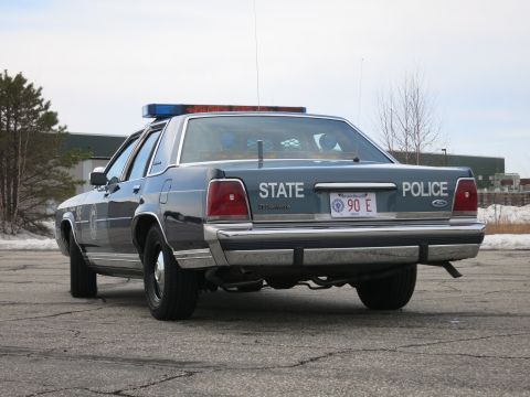 1991 Ford LTD Crown Victoria - Rear three-quarter view of a two-tone blue Ford LTD Crown Victoria State Police cruiser with dual exhaust and a roof light bar.