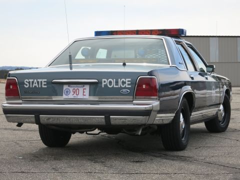 1991 Ford LTD Crown Victoria - Rear three-quarter view of a two-tone blue Ford LTD Crown Victoria State Police cruiser showing the round door emblem and light bar.