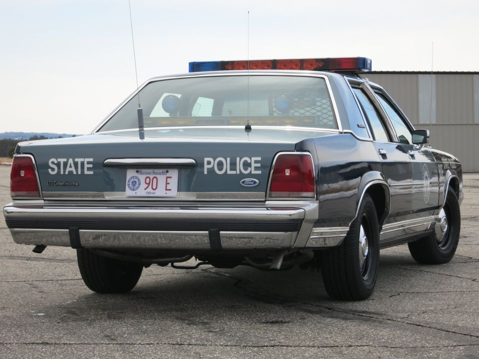 Rear three-quarter view of blue Ford Crown Victoria State Police cruiser with door emblem