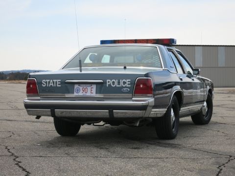 1991 Ford LTD Crown Victoria - Rear three-quarter view of a two-tone blue Ford LTD Crown Victoria State Police cruiser on a wide paved lot.