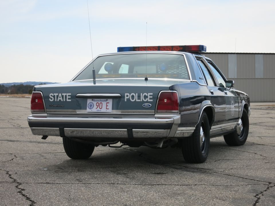 Rear three-quarter view of blue Ford Crown Victoria State Police cruiser on open lot
