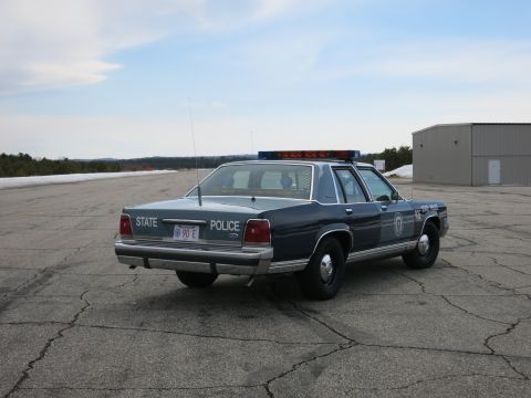 1991 Ford LTD Crown Victoria - Rear three-quarter view of a two-tone blue Ford LTD Crown Victoria State Police cruiser with door emblem on a paved lot.