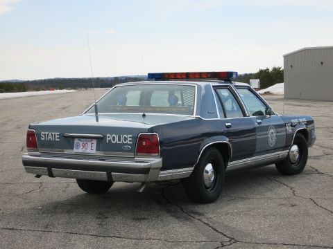 1991 Ford LTD Crown Victoria - Rear three-quarter view of a two-tone blue Ford LTD Crown Victoria State Police cruiser with steel wheels and roof light bar.