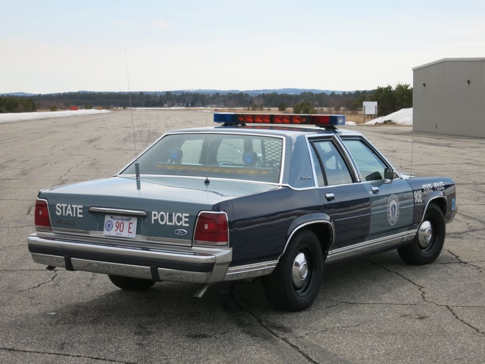 Rear three-quarter view of blue Ford Crown Victoria State Police cruiser with door emblem