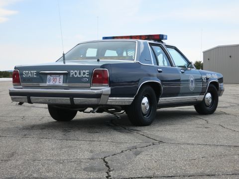1991 Ford LTD Crown Victoria - Rear three-quarter view of a two-tone blue Ford LTD Crown Victoria State Police cruiser with dual exhaust on a cracked lot.