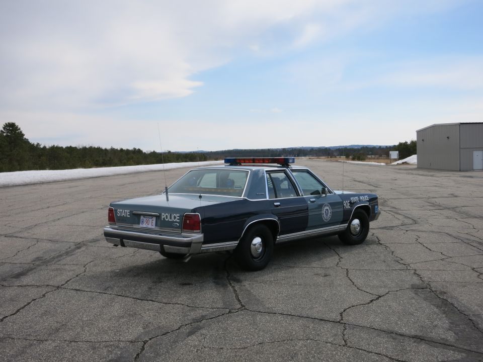 Side-rear view of blue Ford State Police cruiser unit 90E on tarmac