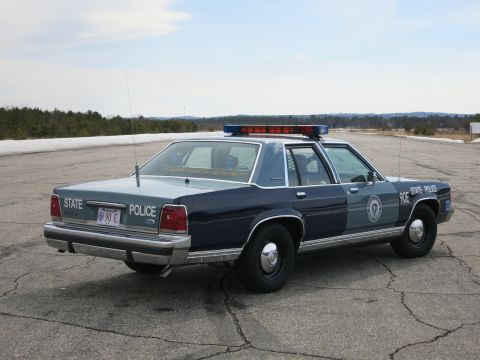 1991 Ford LTD Crown Victoria - Rear three-quarter view of a two-tone blue Ford LTD Crown Victoria State Police cruiser marked 90E STATE POLICE on a paved lot.