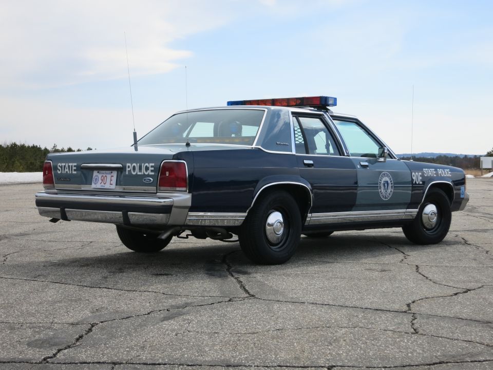 Rear three-quarter view of dark blue Ford Crown Victoria State Police cruiser 90E