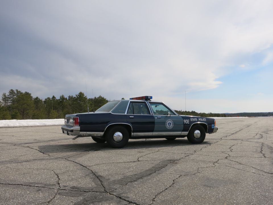 Front-right side view of blue Ford State Police cruiser 90E on open tarmac