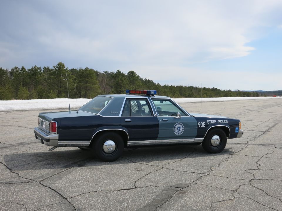 Dark blue Massachusetts State Police sedan, unit 90E, rear three-quarter view in paved lot