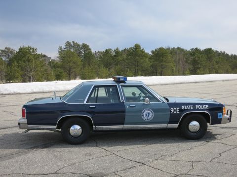 1991 Ford LTD Crown Victoria - blue Massachusetts State Police cruiser marked 90E with a front push bumper, shown in profile near snowbanks.