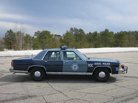 1991 Ford LTD Crown Victoria - Far-side profile of a two-tone blue Massachusetts State Police sedan marked 90E with a push bumper in a paved lot.