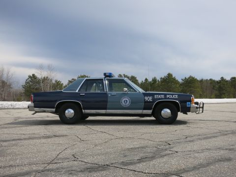 1991 Ford LTD Crown Victoria - Side view of a two-tone blue Massachusetts State Police sedan marked 90E with a front push bumper near snowbanks.